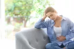 Mujer con dolor menstrual a causa de la endometriosis Mujer joven sentada en un sofá se toca el vientre dolorido