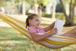 Aprender durante las vacaciones sin ir a la escuela Nia rubia tumbada en verano en una hamaca leyendo un libro