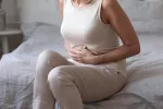 Mujer de mediana edad sufre de trastornos digestivos Mujer de mediana en la edad sentada en la cama con las manos en el abdomen dolorido