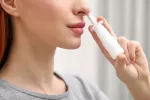 Mujer se aplica espray nasal antialérgico frente al coronavirus Mujer aplicándose un espray nasal para protegerse de enfermedades