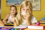 Vuelta al cole para niños alérgicos y asmáticos Niña en el colegio se suena los mocos con un pañuelo