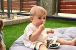 Niño pequeño come arándanos que coge de un plato Un bebé come arándanos sentado sobre una colcha en el jardín