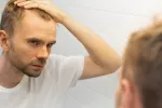 Hombre se mira al espejo con gesto de preocupación por la pérdida de pelo Hombre comprueba en el espejo que está perdiendo cabello