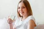 Una joven sostiene un vaso de agua Chica joven sonríe a la cámara sosteniendo un vaso de agua