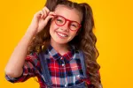 Niña con gafas sonríe a la cámara Niña sonríe sujentado sus gafas