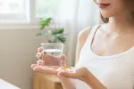 Mujer joven en camiseta de tirantes sostiene un vaso y una vitamina D en la otra mano