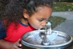 Niña bebiendo agua de una fuente pública