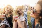 Tres chicas muy sonrientes en un parque sostienen vasos de cerveza