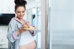 Mujer embarazada sale de la cocina con un plato de pasteles en la mano