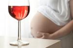 Mujer embarazada con las manos sobre el vientre junto a una copa de vino, en primer plano, sobre una mesa