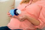 Mujer embarazada sostiene en sus manos un frasco con un suplemento vitamínico