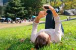 Mujer consulta su smartphone tumbada en el césped en un parque