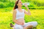 Una embarazada bebe agua de una botella de plástico