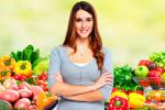 Mujer posa delante de un puesto lleno de frutas y verduras