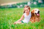 Niña sonríe sentada junto a su perro en el campo