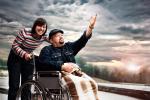 Una mujer sonriente empuja la silla de ruedas de un paciente con ELA