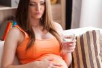 Mujer embarazada sostiene un vaso de agua con gesto preocupado