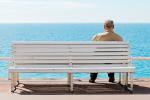 Anciano solo sentado en un banco frente al mar