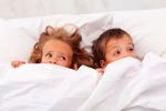 Niña y niño asustados en la cama tapándose la boca con la sábana