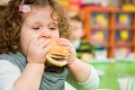 Niña con obesidad infantil comiendo una hamburguesa