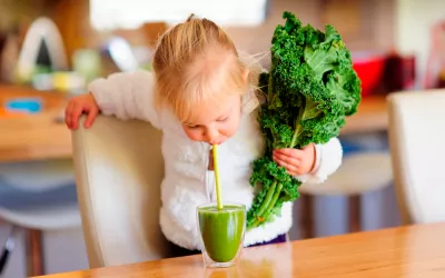 Kale, un alimento muy nutritivo y bajo en calorías Una niña sujeta una col rizada en la mano mientras bebe un zumo de kale