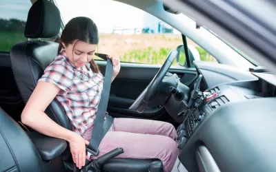 Cómo sentarte al volante para evitar lesiones y accidentes Mujer sentada en el coche colocándose el cinturón de seguridad para evitar lesiones y accidentes.