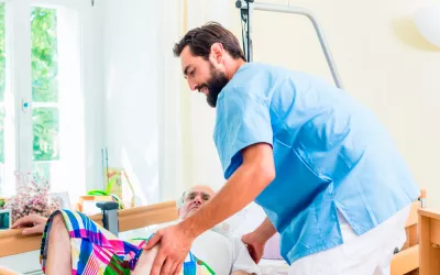 Cómo movilizar a una persona mayor encamada Un cuidador atiende a una persona mayor encamada