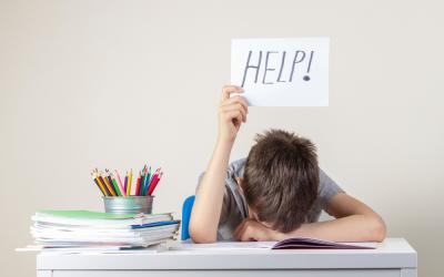 Niño sentado en su escritorio con la cabeza agachada y pidiendo ayuda