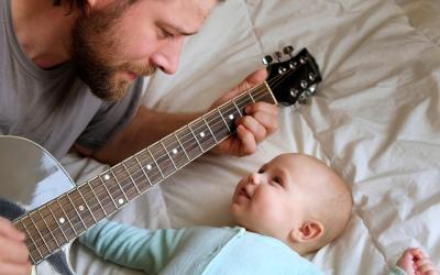 Padre toca la guitarra para su bebé en la cama