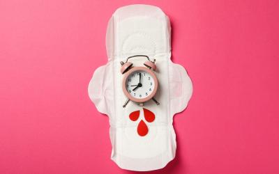 Un reloj somre una compresa simbolizando el tiempo para la próxima mestruación