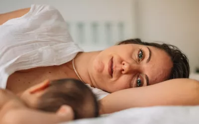 Test ¿Sufres depresión posparto? Mujer tumbada en la cama con la mirada perdida junto a su bebé recién nacido