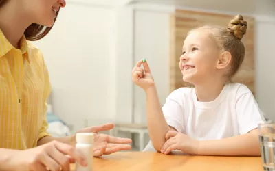 Suplementos vitamínicos en los niños Madre le da una vitamina a su hija pequeña que la coge sonriendo