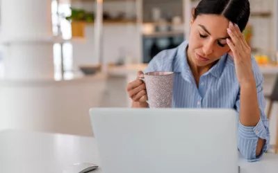 A una mujer con una taza de café le cuesta prestar atención a la pantalla de su ordenador Mujer con aspecto cansado sostiene una taza de café frente a su portátil