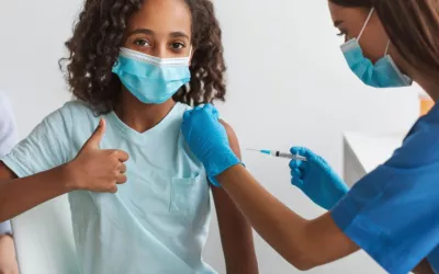 Sanitaria vacunando a una niña contra el COVID-19 Niña hace un gesto de aprobación con el pulgar mientras es vacunada