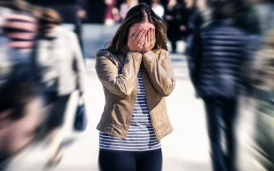 Mujer joven sufre un ataque de ansiedad o crisis de pánico rodeada de gente Joven se tapa la cara rodeada de gente en la calle