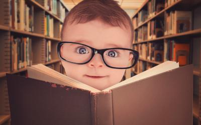 Un bebé con gafas frente a un libro abierto