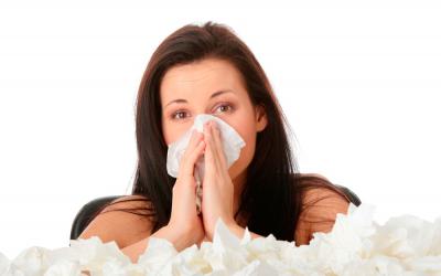 Una mujer con rinitis se suena la nariz junto a una pila de pañuelos de papel usados