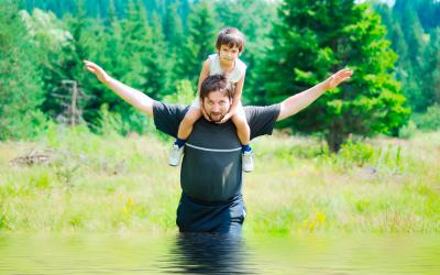Un hombre cruza un arroyo con su hijo a hombros