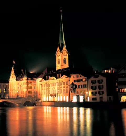 Vista nocturna sobre el río Limmat de la casa 'Zur Meise', la torre de la iglesia Fraumuenster y el Ayuntamiento. @ ST/SwissImage.